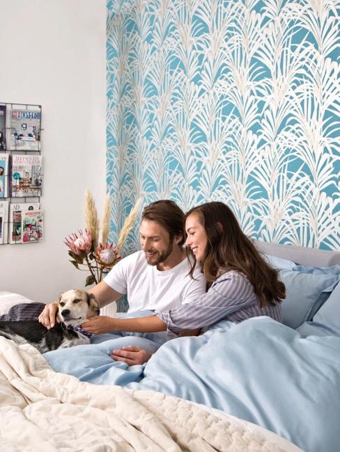 Pärchen mit Hund im Bett Pärchen mit Hund im Bett vor blau gemusterter Tapete