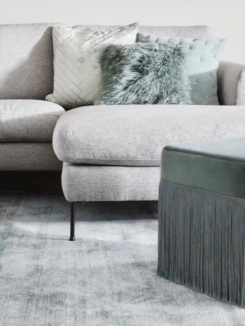 Graues Ecksofa dekoriert mit pastellgrünen Kissen und Samt-Fransen-Pouf neben Marmor Couchtisch Lesley.
