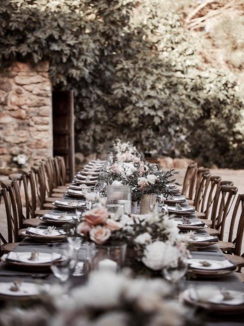 Grande tavolo da pranzo all'aperto coperto con fiori e segnaposto