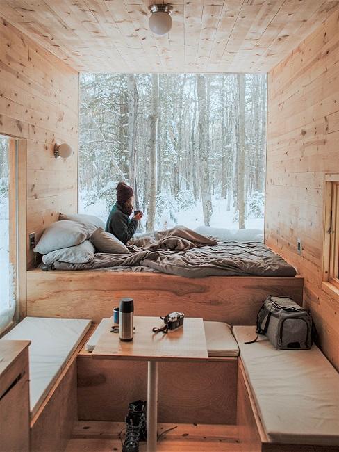 Eine Frau sitzt auf dem Bett in einem Tiny House und blickt aus dem Fenster.