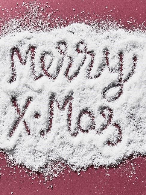 Merry X-mas Merry X-Mas in Schnee geschrieben auf rotem Tisch