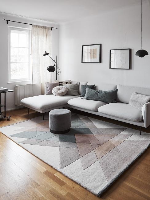 günstig einrichten Wohnzimmer mit einem großen grauen Sofa, einem gemusterten Teppich, zwei Wandbildern, Dekokissen und schöner Beleuchtung