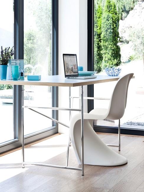 Ein Schreibtisch vor einer Fensterfront in der Ecke, dazu ein moderner Designerstuhl in Weiß