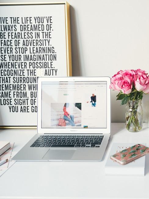 Bilder fürs Büro Schreibtisch mit Laptop, Blumen und einem Wandbild im Rahmen, einfach nur angelehnt an die Wand