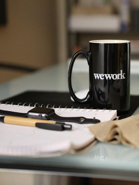 Kleines Büro einrichten Schreibtisch mit schwarzer Tasse mit der Aufschrift "We work" neben einem Block und Stiften