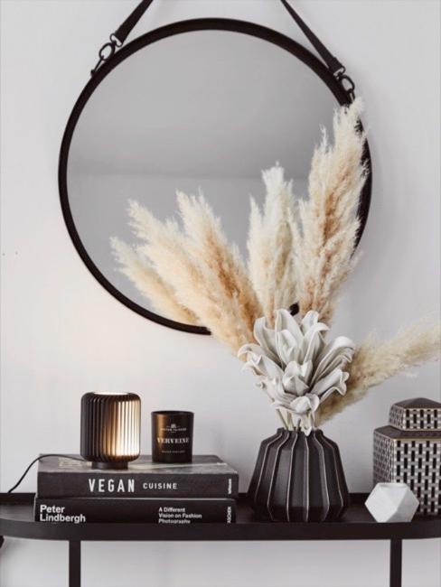 L’herbe de la pampa L'herbe de la pampa claire en vase noir sur buffet noir avec livres déco et miroir mural rond.