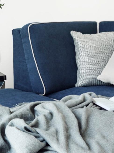 Czyszczenie tapicerki meblowej Tapicerowana sofa w kolorze granatowym z szarymi poduszkami i kocem