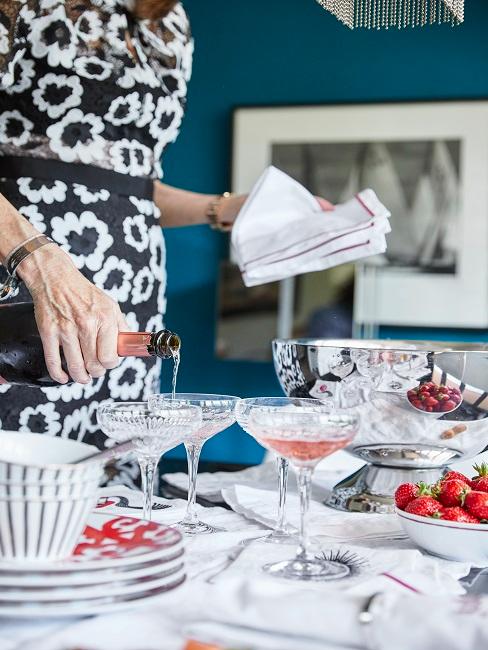 Frau schenkt Champagner in Champagner Schalen auf Esstisch