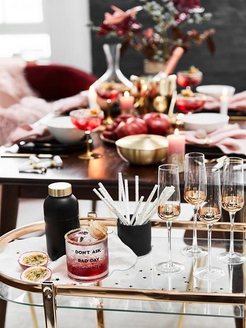 Cocktail party Wózek barowy z 4 kieliszkami do szampana i zastawionym stołem w tle.