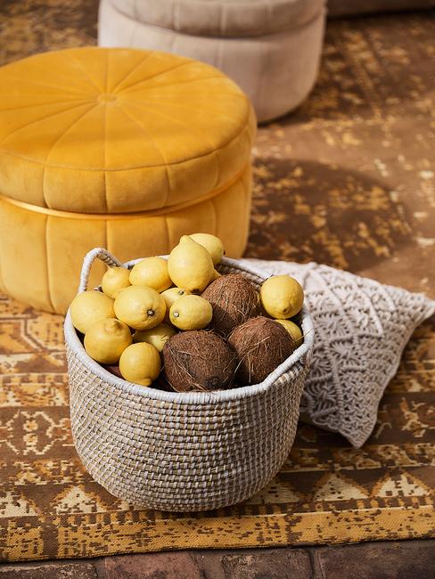 deco-jaune-citron Pouf jaune foncé sur un tapis ochre devant un panier en cannage avec des citrons à l'intérieur