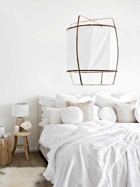 Lit blanc défait avec plusieurs coussins et un lampadaire blanc et or