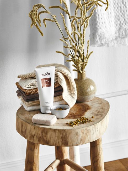 Plante en vase sur un tabouret en bois avec des crèmes dans une salle de bains