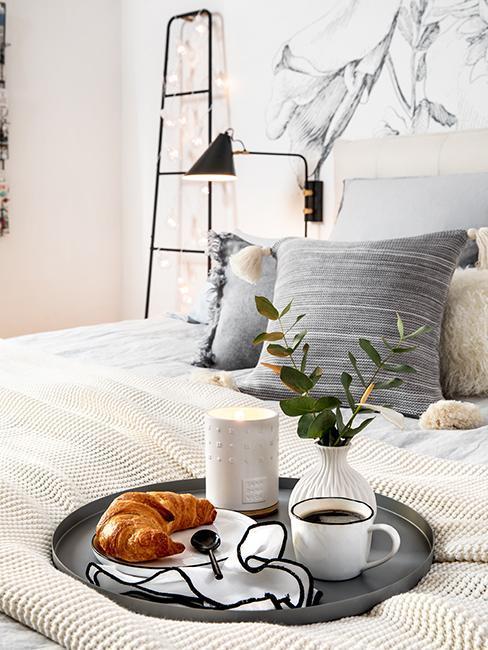 petit-dejeuner-au-lit Plateau de petit déjeuner avec croissant, tasse de café et verre de lait placé sur un lit
