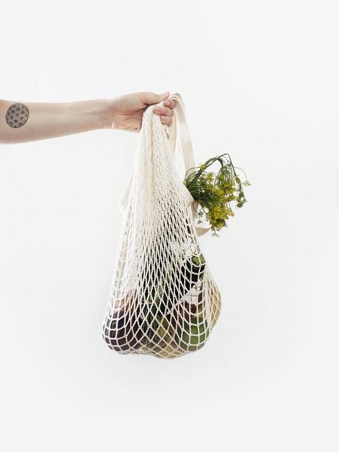 Zero Waste Frauenarm, der einen Netzbeutel mit unverpackten Lebensmitteln in der Hand hält