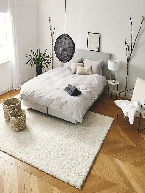 Feng Shui Schlafzimmer mit weißem Bett, weißem Teppich, Körben, schwarzer Lampe, weißem Sessel und Deko-Ästen