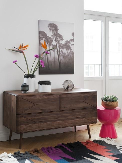 Stilmix Kubanisch mit Vontage Sideboard aus dunklem Holz, Dekovasen und Blumen, bunter Teppich und roter Hocker