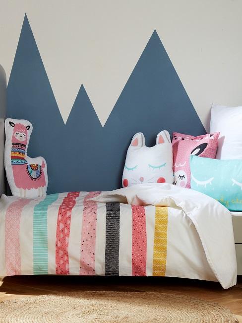 Kinderbett mit verspielten Kissen vor Wand mit blauen Bergen