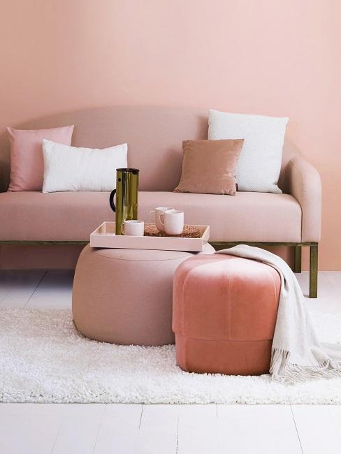 Wohnzimmer mit pastellrosa Wand, rosa Sofa, Poufs, Kissen und weißem Teppich
