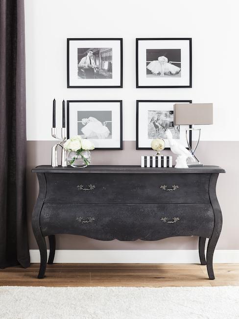 Cómoda de madera oscura en un pasillo con velas y una lámpara encima, y en la pared cuatro fotos enmarcadas en fondo blanco