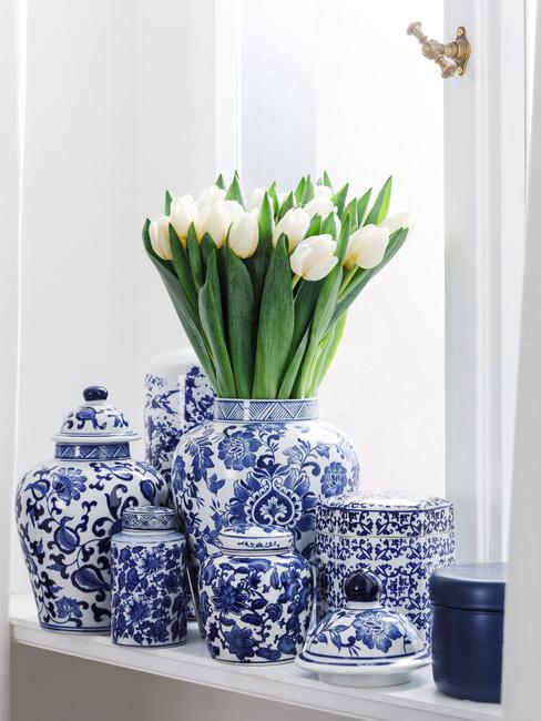 Wiosenne kwiaty Zbliżenie na parapet na którym znaduje się biało-niebieska porcelana oraz białe tulipany