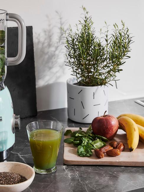 Przepisy na smoothie Szklanka z zielonym sokiem stojąca obok drewnianej deski z owocami oraz oregano w doniczce