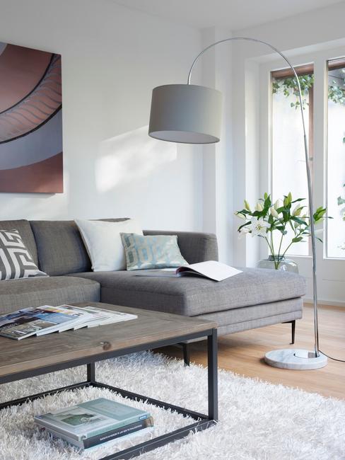 Szary salon z kanapą narożą, dużą, stojącą lampą oraz stolikiem kawowym