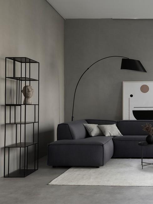 Fragment salonu z narożną kanapą, dużą, stojącą lampą oraz czarnym, metalowym regałem z dekoracjami w stylu industrialnym