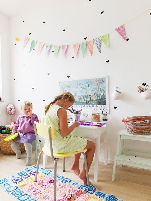 Salle de jeux Grande fille assise au bureau en train de dessiner, petite fille assise à côté en train de jouer