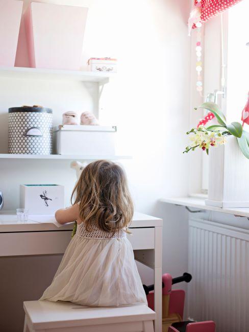 École à domicile Petite fille assise à son bureau blanc avec boîtes de rangement blanches et fleurs dans un vase blanc