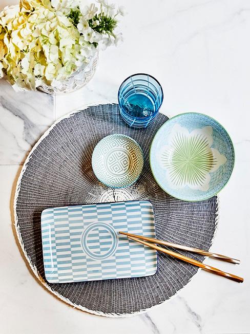 Asiatische Tischdeko in Blau und Grün auf Tisch mit Essstäbchen neben Pflanze