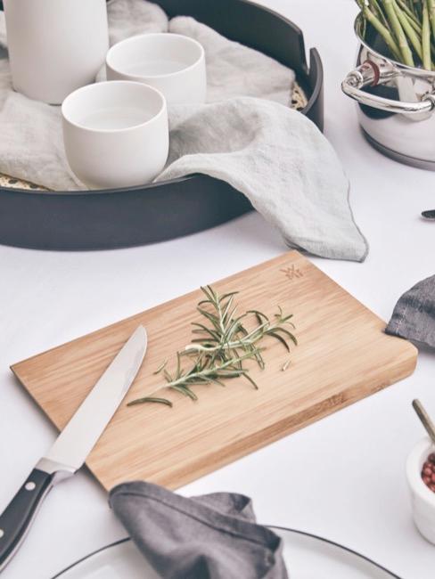 una tabla de cortar de madera, un cuchillo, una bandeja con vajilla blanca