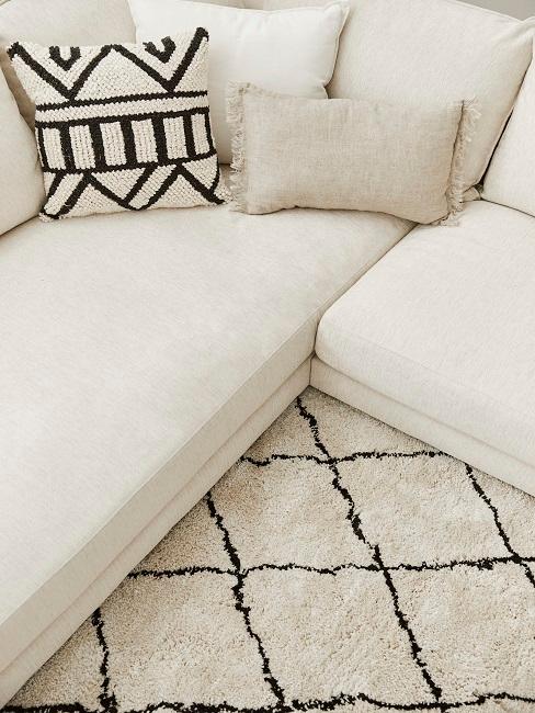 Ein beiges Sofa mit einem gemusterten Kissen auf einem schwarz-beige-gestreiftem Teppich