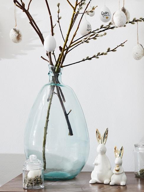 Große Vase mit Osterzweigen neben weiß-goldenen Osterhasen