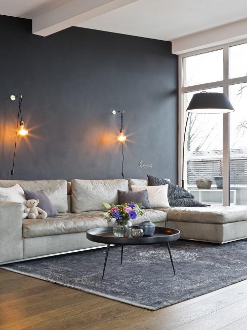 Schwarze Wandfarbe im Wohnzimmer mit beigen Sofa, dunklem Teppich und Wandleuchten