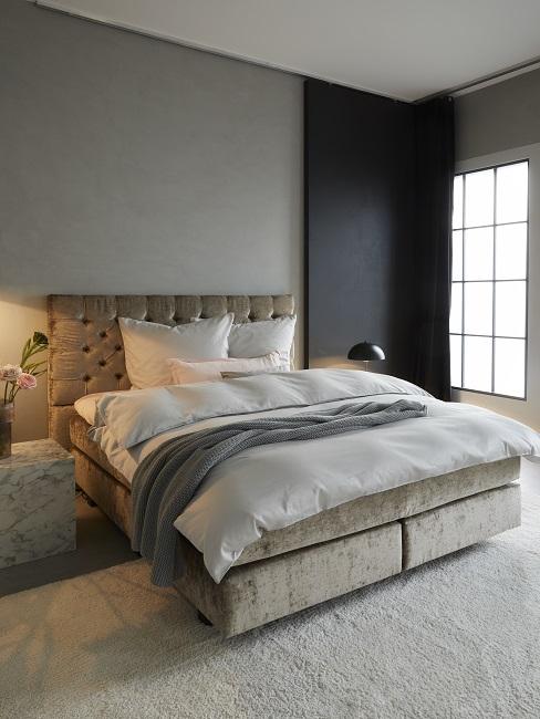 Schlafzimmer mit grauer und schwarzer Wand, beigem Bett und hellgrauem Teppich