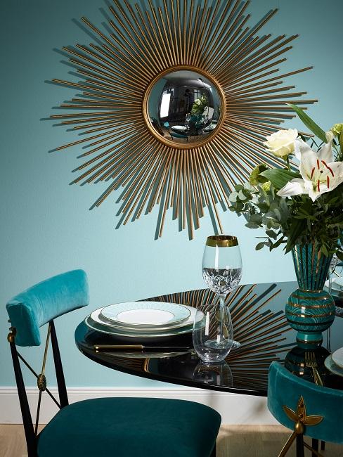 Esszimmer mit goldenem Sonnenspiegel, schwarzen Glanztisch mit Tischdeko, Vase und Samtstühlen in Türkisblau