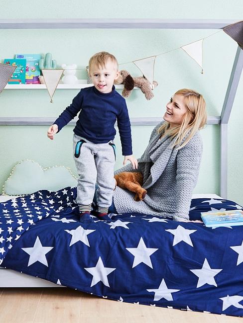 Kind mit Frau auf Bett mit blauer Bettwäsche mit Sternen