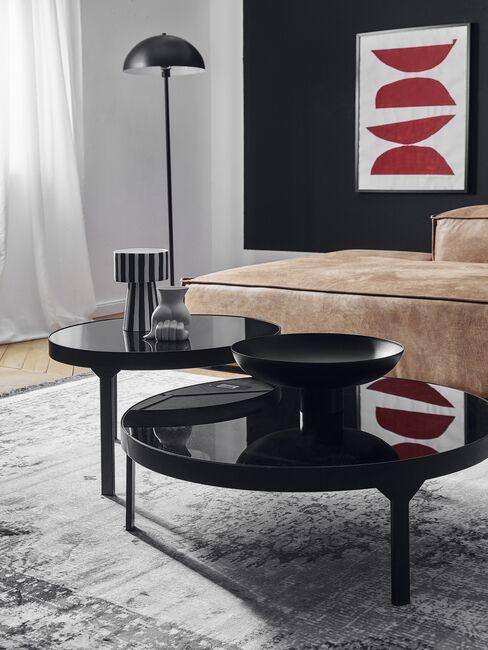Czarne stoliki kawowe przy jasnej sofie na tle ciemnej ściany z designerską grafiką