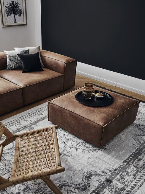 Sofa i puf z jasnej skóry oraz rattanowy fotel w salonie z ciemną ścianą