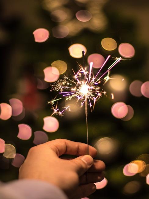 neujahrswünsche Eine Hand, die eine funkelnde Wunderkerze gegen die Dunkelheit hält