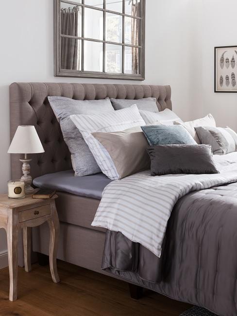 schlafzimmer landhausstil Bett in Grau mit Kissen im Landhausstil und einem Holz-Vintage-Beistelltisch sowie einem Spiegel im Fensterstil
