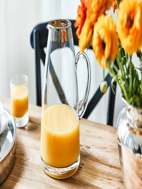 Zumos caseros Vaso y jarra con zumo de naranja encima de una mesa de madera junto a un jarrón de flores