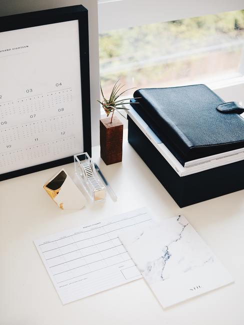 Huishoudboekje 10 Witte tafel met notitieboeken en kalender in zwart fotolijstje