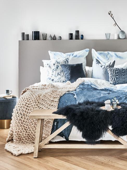 Cama decorada con mantas en tonos distintos de azul petróleo y gris
