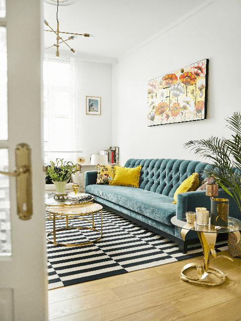 Wohnen im 70s Style Wohnen im 70s Style: Wohnzimmer mit blauer Couch, gelben Kissen, schwarz-weiß Teppich, Pflanze und Bild