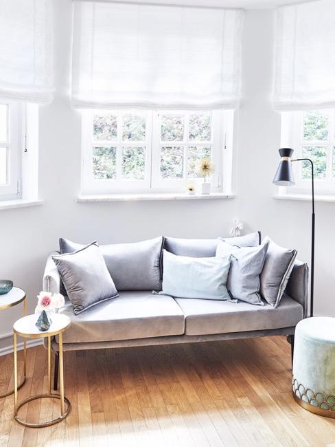 sala de ocio habitación con ventanas grandes, sofá de coor azul claro con cojines, un puf y lámpara de pie