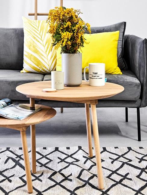 Graues Sofa mit gelben Kissen hinter Beistelltischen mit gelben Blumen in grauer Vase