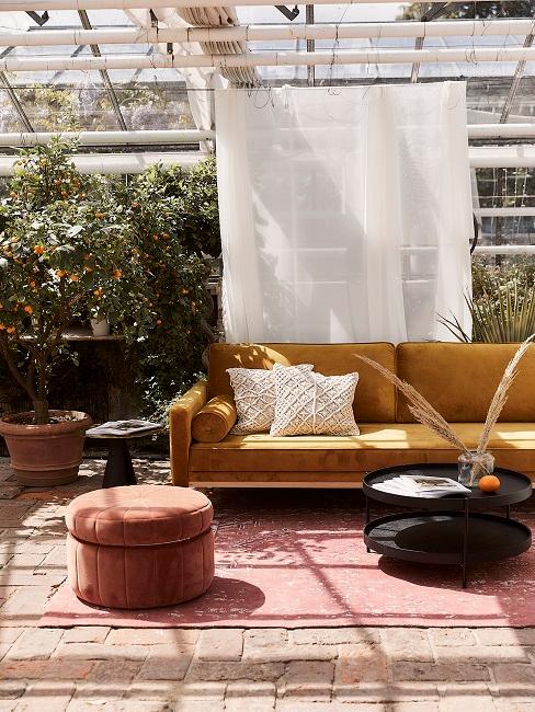 Gelbes Samtsofa im Outdoorbereich mit Pflanzen und rotem Pouf