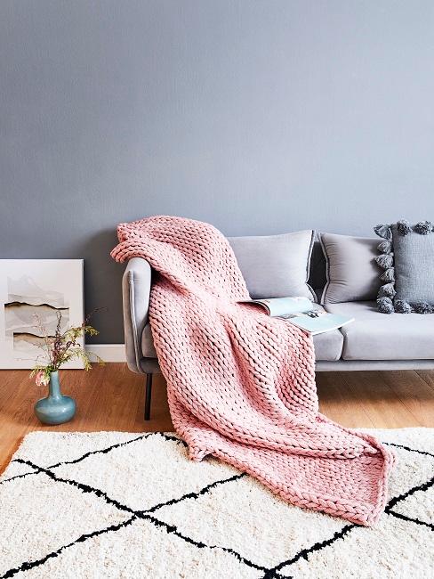 Grau-blaue Wand hinter grauem Sofa mit rosa Decke und cremefarbenem Teppich