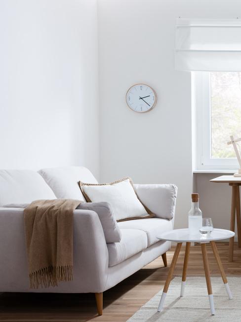 Salon z stylu nowoczesnym z asną kanapą, drewnianym stolikiem oraz zegarem na ścianie